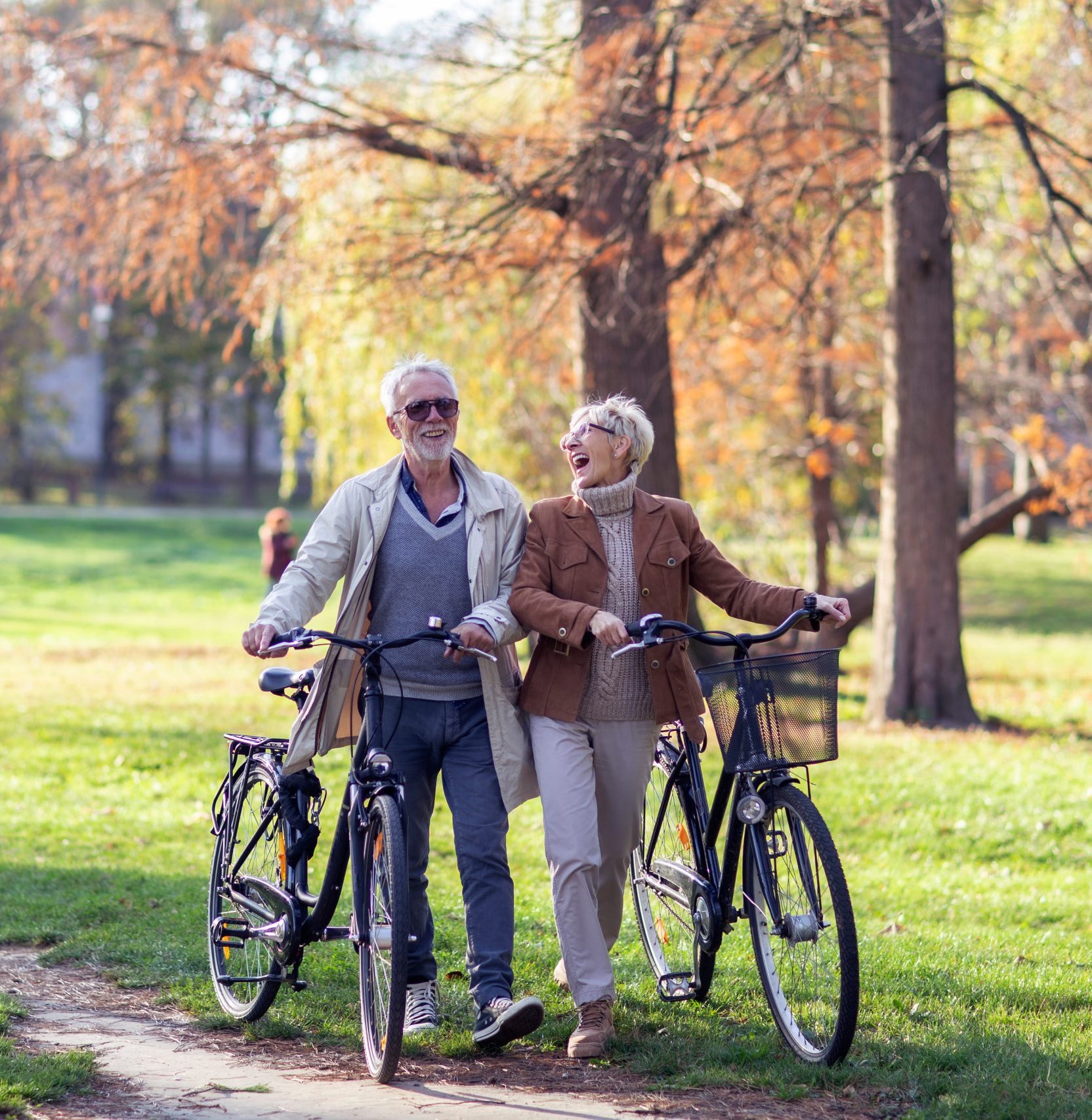 Mature fit couple pushing bicycles in public park talk and smile